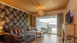 Un salon moderne avec un plafond en bois, un canapé, une table basse et une grande fenêtre avec des rideaux.