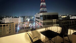 A rooftop terrace with a view of a lit tower, a building, and a cityscape at night. - JRE Cozy Rooftop Near Al Services-23 (Amman)