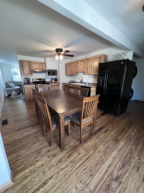 A spacious kitchen with wooden cabinets, a dining table with chairs, a black refrigerator, and a ceiling fan. - Cozy home near Lake Michigan with Smart TVs, fast Wi-Fi, and rustic charm. (Michigan City)
