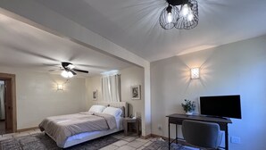 Ein Schlafzimmer mit einem Bett, einem Schreibtisch, einem Sessel, einem Fernseher, einem Deckenventilator und Wandleuchten.
