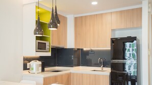 Una cocina moderna con armarios de madera, microondas integrado, refrigerador de acero inoxidable e iluminación colgante.