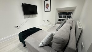 A modern living room with a grey sofa, a black TV mounted on the wall, and a framed picture above the sofa. - Beautiful 2 Bed Apartment in Walton on the Naze (Walton on the Naze)