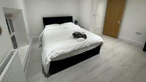 A modern bedroom with a large bed, a wooden door, and a radiator. - Beautiful 2 Bed Apartment in Walton on the Naze (Walton on the Naze)
