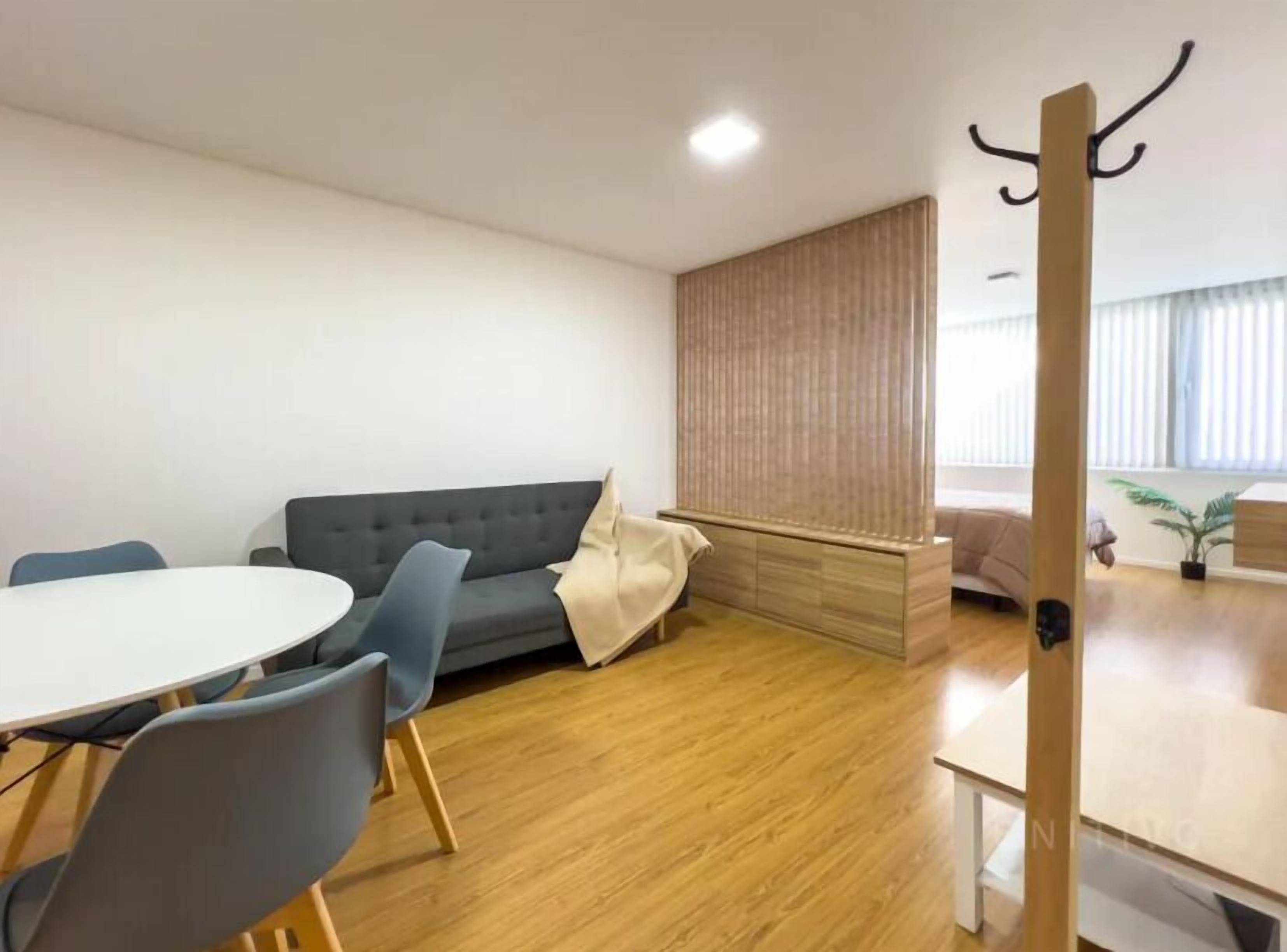 A modern living room with a grey sofa, a round dining table with chairs, and a wooden floor.