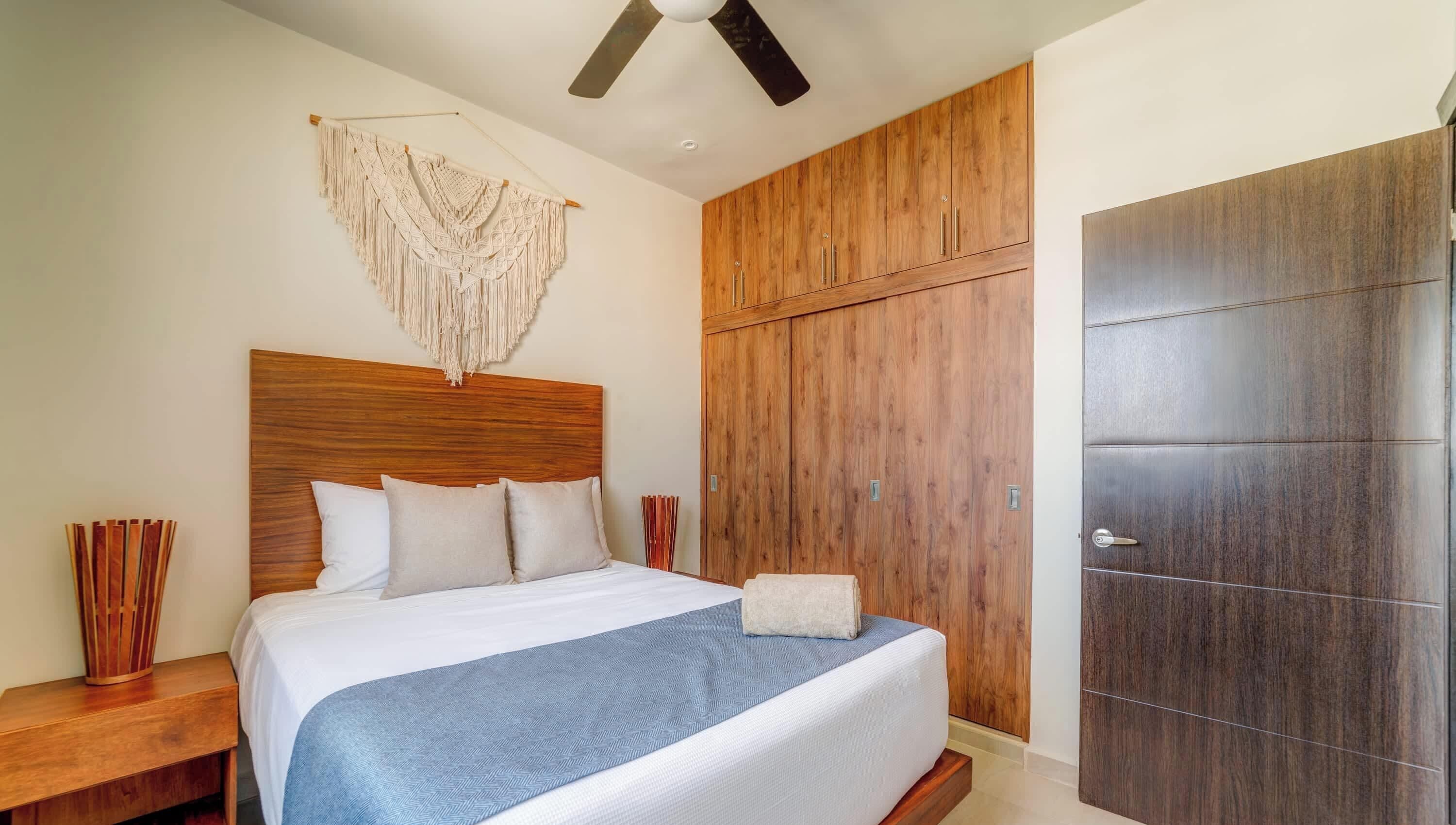 Una camera da letto con una testiera in legno, un letto con biancheria da letto bianca, una coperta azzurra, un armadio in legno e una ventola a soffitto.