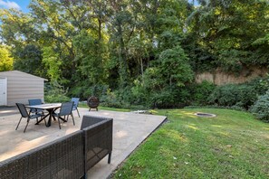 Un patio con muebles de exterior, una chimenea y un área verde con árboles.