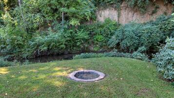 Un jardin aménagé avec un foyer circulaire, une végétation luxuriante et un ruisseau.