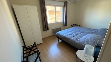 Una camera da letto con un letto, un armadio, un termosifone, una finestra con tende, una sedia e un tavolo con una lampada.