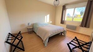 Une chambre à coucher avec un lit, une table de chevet, une lampe, une fenêtre avec des rideaux et un radiateur.