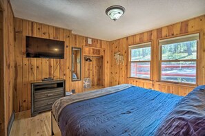 A wooden-paneled bedroom with a bed, dresser, TV, and windows. - Cozy Mountain Retreat at the Base of Pikes Peak! (Cascade-Chipita Park)