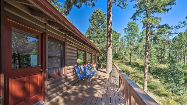 Eine Holzhütte mit einer Holzterrasse, einer roten Tür und blauen Stühlen.