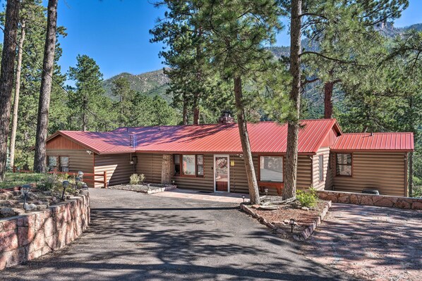 A log cabin with a red roof, surrounded by trees and a mountain in the background. - Cozy Mountain Retreat at the Base of Pikes Peak! (Cascade-Chipita Park)