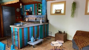 Une cuisine avec un mur de crédence à rayures colorées, un coin repas en bois avec des chaises bleues et un petit bar avec des tabourets.
