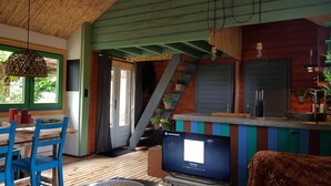 Une pièce chaleureuse avec un plancher en bois, une télévision, un escalier et une fenêtre avec des rideaux.