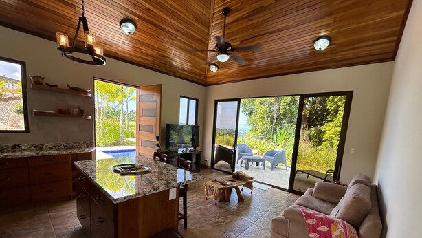 A spacious living area with a kitchen, a large TV, and a sliding glass door leading to a patio. - Villa Romancing The Stone - Amazing Villa in Ojochal, Osa (Ojochal)