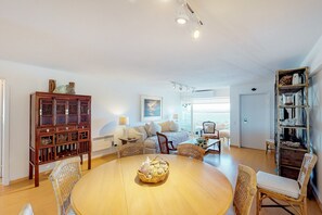 Un vaste espace de vie comprenant une table ronde en bois, des chaises en osier, un meuble en bois et une bibliothèque.