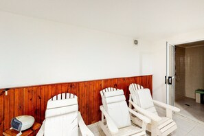 Une pièce avec des chaises blanches, un mur en bois, une petite table avec une radio et une porte donnant sur un espace douche.