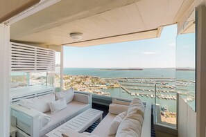 A balcony with a white sofa, a small table, and a view of a marina with boats and a distant shoreline.