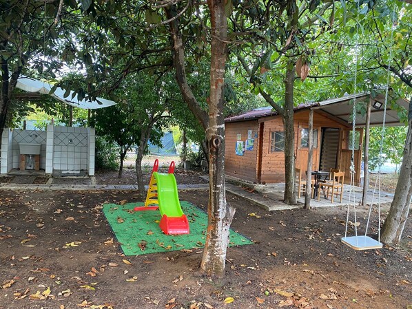 A playground with a slide and swings, a small wooden building, and a covered seating area.