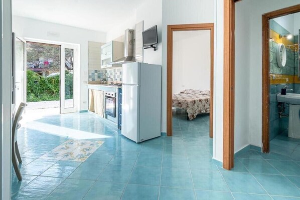 A modern kitchen with a refrigerator, stove, and microwave. There is a dining area with a table and chairs. The room has a large window and a door leading to a balcony. - Villa Anna - Holiday House Palinuro (Campania)