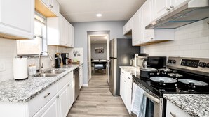 A modern kitchen with white cabinetry, granite countertops, a stainless steel refrigerator, and a black stove. - Cozy & Bright 4BR Home - Perfect for Families (Watauga)