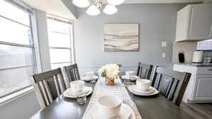 A dining area with a long table set for six, flanked by chairs, a vase with flowers, and a painting on the wall. - Cozy & Bright 4BR Home - Perfect for Families (Watauga)