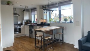 A modern kitchen with a central island, bar stools, and a view of the city through large windows. - Two bedroom flat in Hoxton, sunny terrace, 10 mins from Old Street tube station (London)