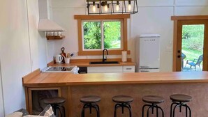 A modern kitchen with a central island, bar stools, a built-in oven, and a window overlooking greenery.