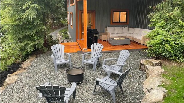 A modern house with a deck, outdoor seating, and a fire pit.