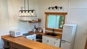 A compact kitchen with a wooden island, bar stools, a microwave, a stove, a sink, and a refrigerator.
