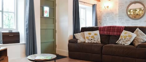 A cozy living room with a brown sofa, colorful rug, and a Singer appliance on the window sill.