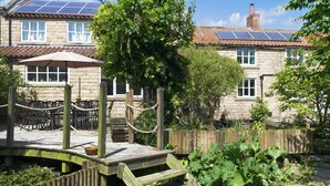 Un bâtiment en pierre doté d’un jardin, d’une terrasse en bois et de panneaux solaires sur le toit.