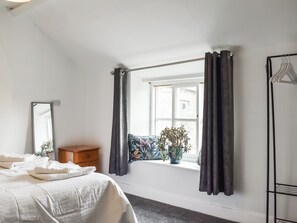 Une chambre à coucher avec un lit, une commode, une fenêtre avec des rideaux et un miroir.