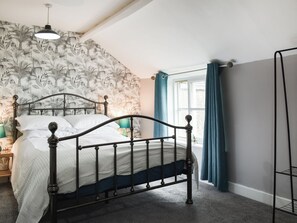 A bedroom with a four-poster bed, a nightstand with a lamp, a window with curtains, and a wall with a floral wallpaper pattern. - 4 bedroom accommodation in Pickering (Pickering)
