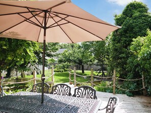 An outdoor patio with a table and chairs under a large umbrella, surrounded by greenery and a wooden deck. - 4 bedroom accommodation in Pickering (Pickering)