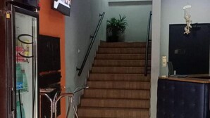 A hotel lobby with a staircase, a vending machine, a television, and a desk. - El Nassr Suits Ltda  (Goiânia)