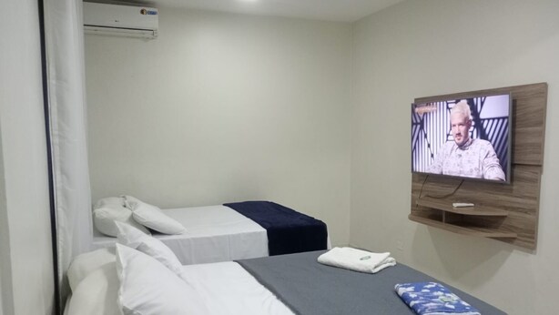 A hotel room with two beds, a TV mounted on the wall, and an air conditioning unit. - El Nassr Suits Ltda  (Goiânia)