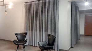 A room with two black leather chairs, a grey curtain, and a wooden door. - El Nassr Suits Ltda  (Goiânia)