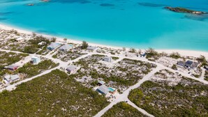 Luchtbeeld van een kustresort met meerdere gebouwen, helder turquoise water en een zandstrand.