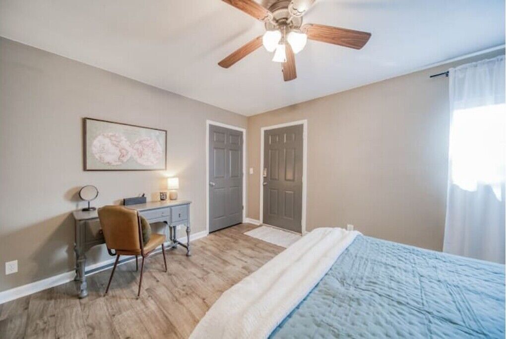 A bedroom with a bed, a desk, a chair, a ceiling fan, and a door.