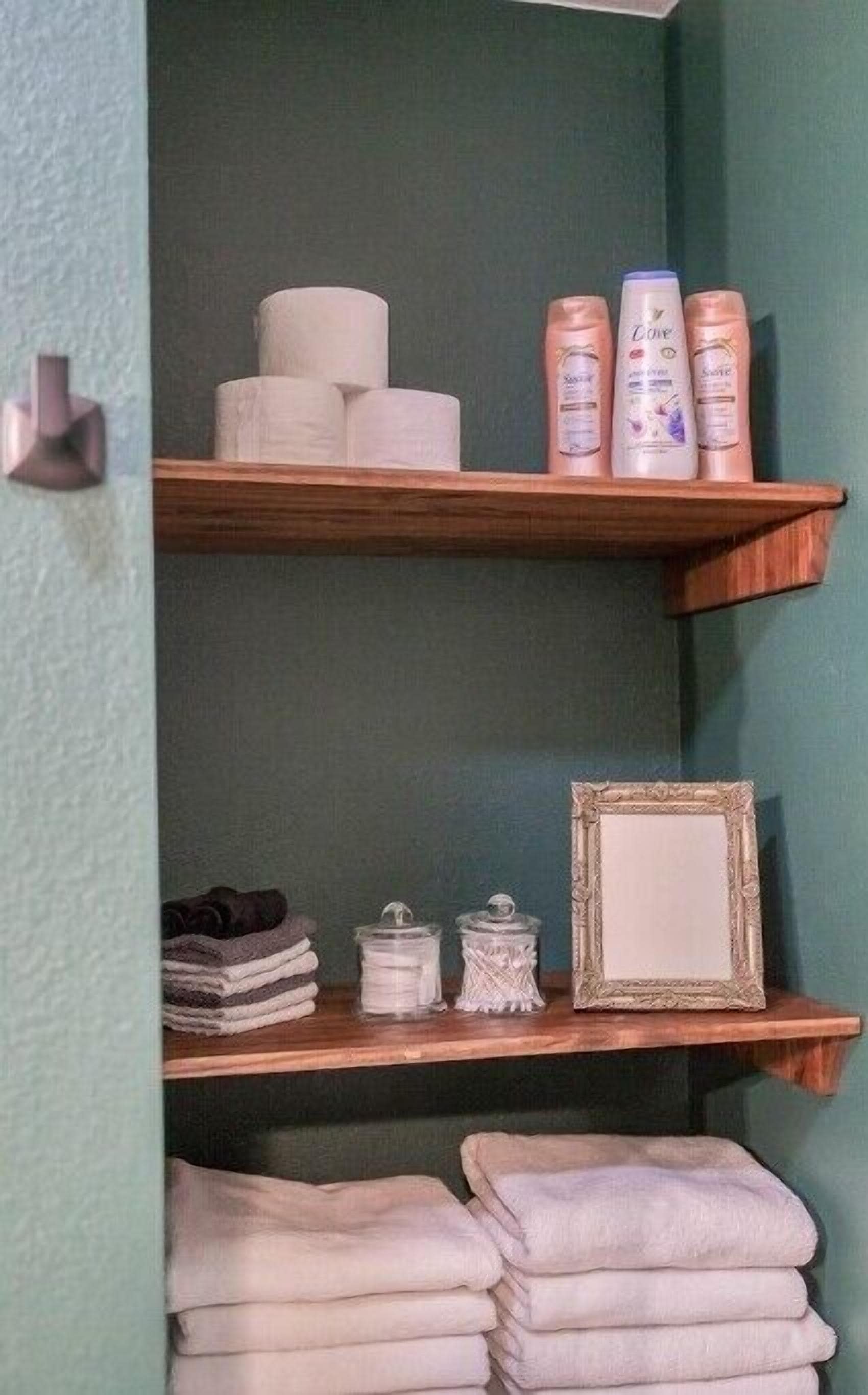 Un baño con estantes de madera que sostienen artículos de aseo, toallas y un espejo enmarcado.