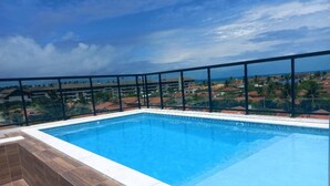 A rectangular swimming pool with a black metal railing, surrounded by a tiled deck. - Cupe Summer 301-Refúgio na Praia-By Use (Ipojuca)