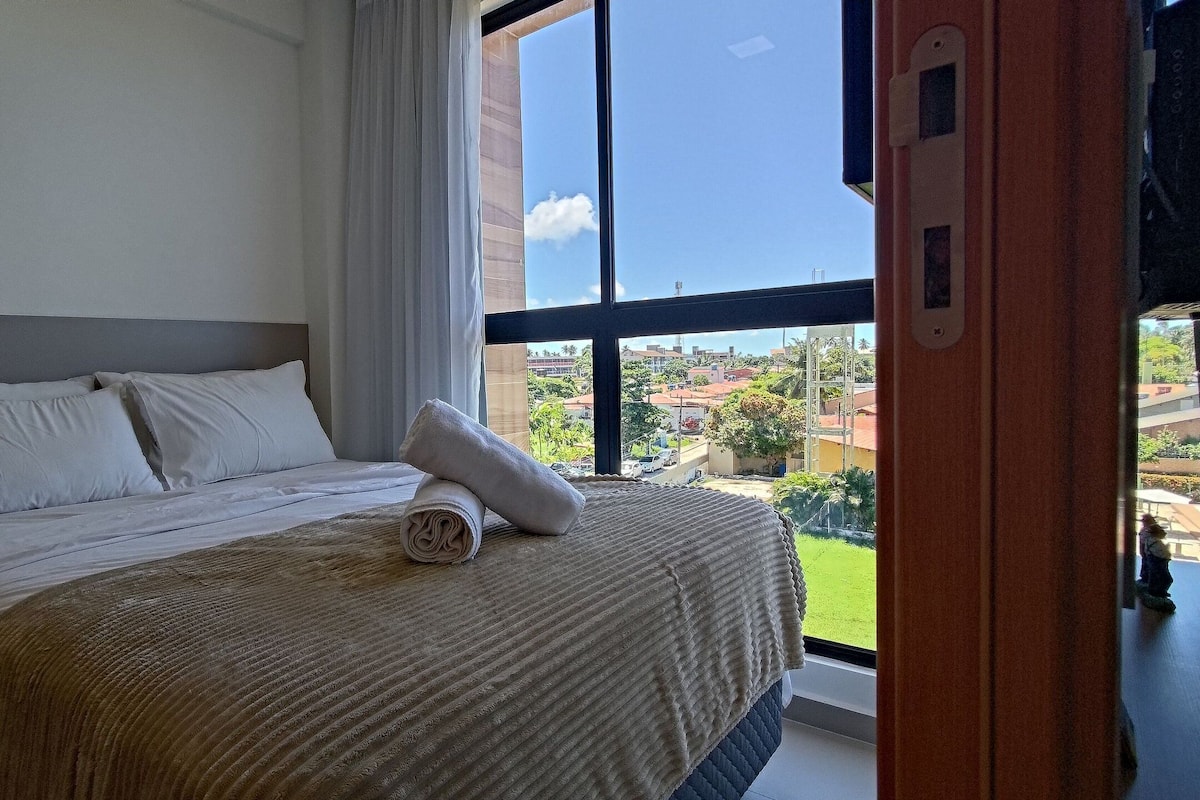 Ein Hotelzimmer mit einem großen Bett, Blick auf die Stadt durch ein Fenster und einem Vorhang.