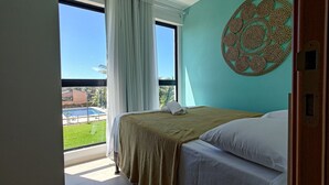 A hotel room with a bed, a view of a swimming pool, and a large window with curtains. - Cupe Summer 301-Refúgio na Praia-By Use (Ipojuca)