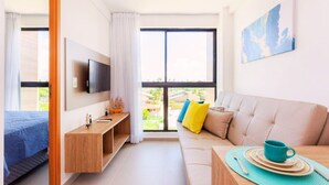 A modern hotel room with a bed, a sofa, a TV, and a view of the outdoors. - Cupe Summer 301-Refúgio na Praia-By Use (Ipojuca)