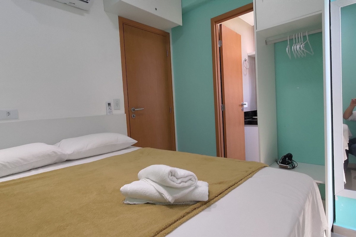 Ein Hotelzimmer mit einem Bett, einer Holztür, einem durch eine offene Tür einsehbaren Badezimmer und einem Handtuch auf dem Bett.