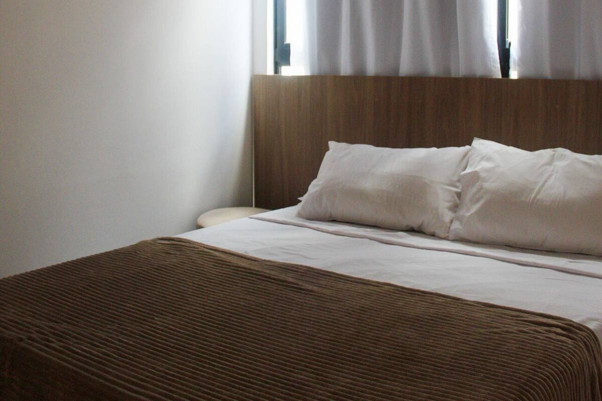 Ein Hotelzimmer mit einem großen Bett, einem Holzkopfteil und einem Fenster mit Vorhängen.