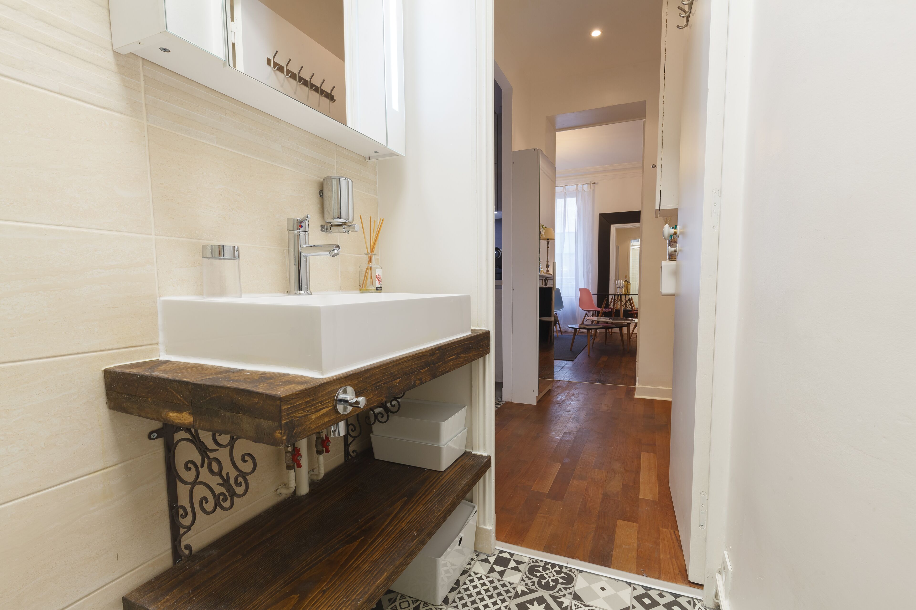 A modern bathroom with a white sink, wooden shelf, and decorative mirror.