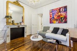Un salon moderne avec un canapé blanc, une table basse en verre, une cheminée et un grand miroir.