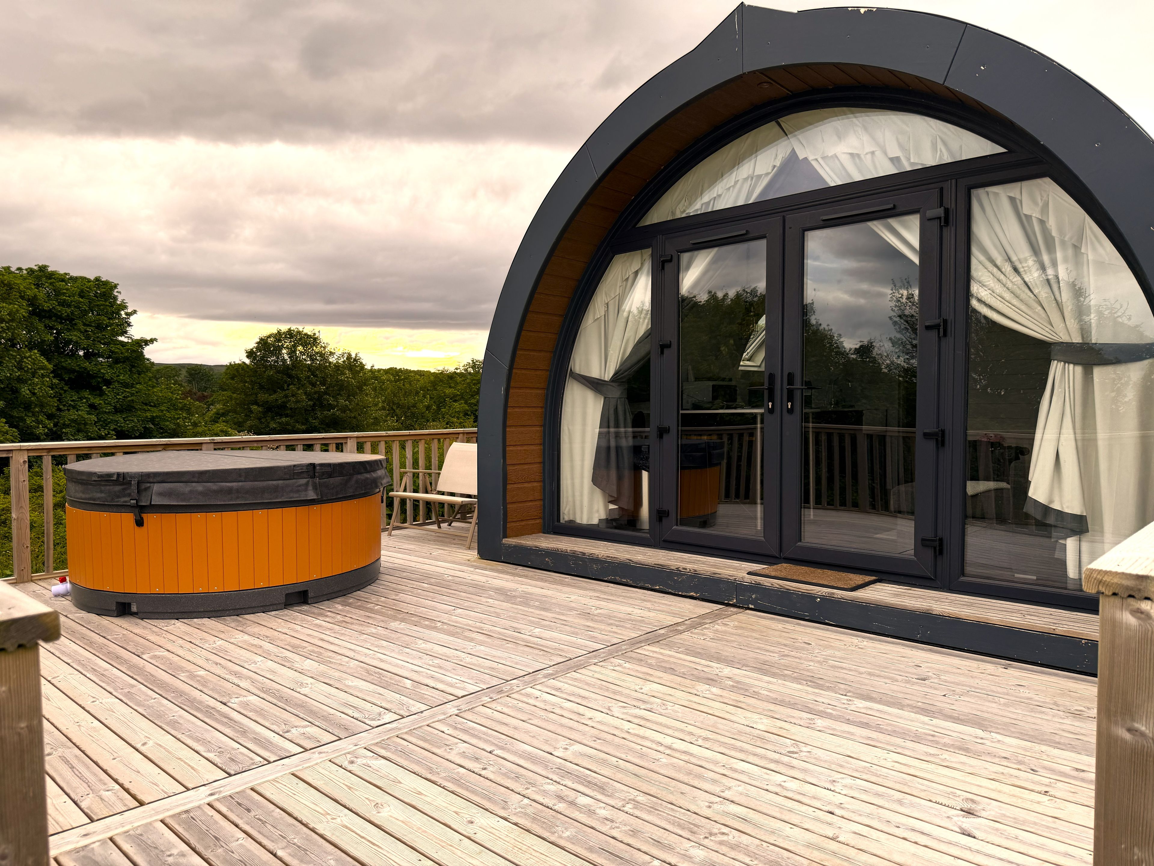 A hot tub on a wooden deck with a glass-enclosed room.